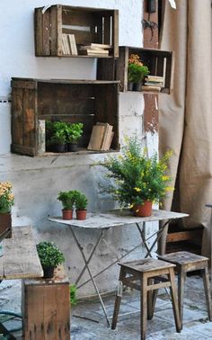 an outdoor table with potted plants and books on the shelf next to it in front of a window