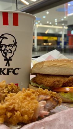 a chicken sandwich and fried food with a cup of kfc on the table in front of it