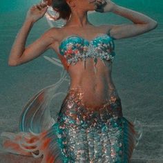 a woman in a blue and silver dress standing on the beach with her hands behind her head