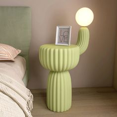 a green table lamp sitting on top of a bed next to a night stand with a picture frame