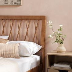 a wooden headboard with white pillows and flowers in a vase on the end table