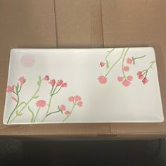 a white plate with pink flowers on it sitting on top of a table next to a cardboard box