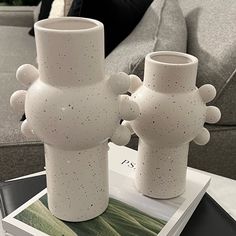 two white vases sitting on top of a table in front of a gray couch