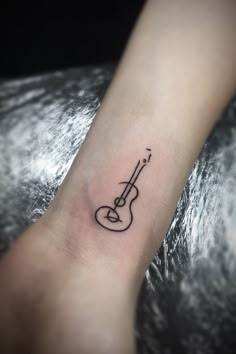 a small guitar tattoo on the wrist is shown in black ink, and it looks like an instrument