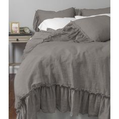 the bed is made with grey linens and ruffled bedspread, along with white pillows