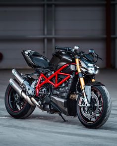 a black and red motorcycle parked in a parking lot next to a garage door with it's lights on