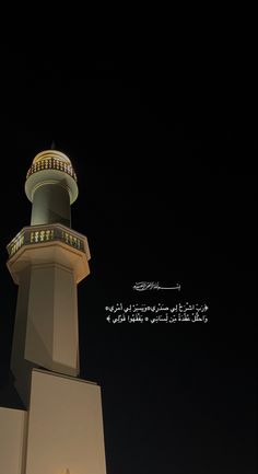 a tall white tower with a clock on it's side and arabic writing in the background