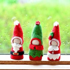 three small christmas gnomes sitting on a window sill in front of a rainy window