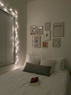 a white bed topped with pillows and blankets next to a window covered in string lights