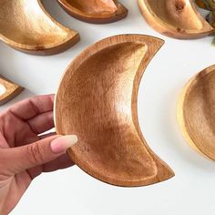 a person is holding a wooden crescent shaped dish in front of some other wood bowls