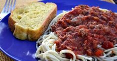 a blue plate topped with spaghetti and meat sauce next to a slice of toasted bread