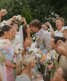 a group of people standing next to each other in front of a wedding cake and flowers