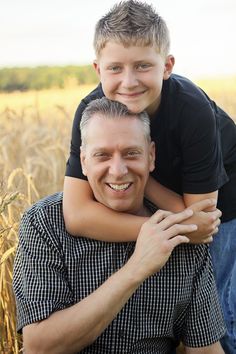 a man holding a young boy on his shoulders in a wheat field with tall grass