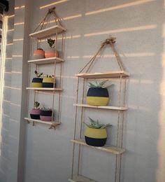 three hanging shelves with pots and plants on them, against a wall in a room