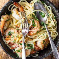 pasta with shrimp and parsley in a skillet on top of a wooden table