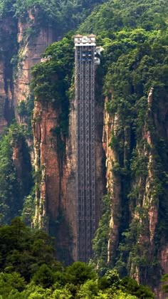 a very tall building sitting on the side of a mountain covered in lush green trees