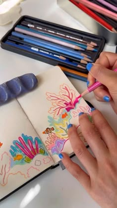 a woman is drawing with colored pencils on a notebook and some other art supplies