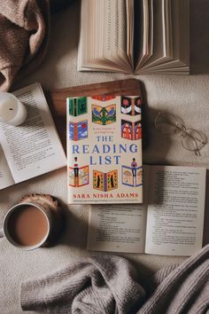 an open book sitting on top of a bed next to a cup of coffee and two books