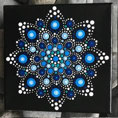 a black and white painting with blue dots on it's center is surrounded by rocks