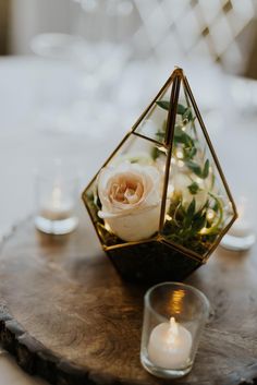 a candle holder with flowers and candles on top of a wooden table in front of a glass vase