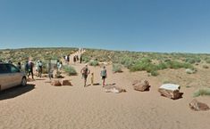 a group of people standing in the desert next to a car and some rocks on the ground