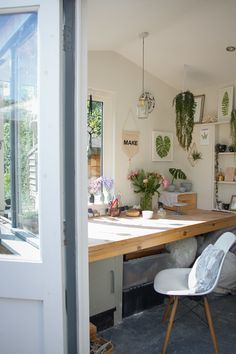 a room with a table, chairs and plants on the wall in it's corner