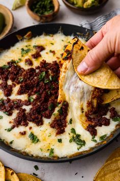 a hand dipping a tortilla chip into a skillet filled with cheese and chili