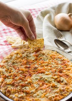 a person dipping a tortilla chip into a casserole dish with onions and cheese