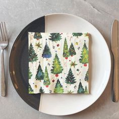 a white plate topped with a napkin covered in christmas tree designs next to silverware