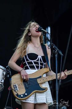 a woman in a dress playing an electric guitar at a music festival with another person standing next to her