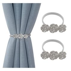 two silver rings with flowers on them are next to a curtain and some draperies