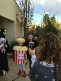 some people in costumes are taking pictures with their cell phones and one is holding a popcorn box