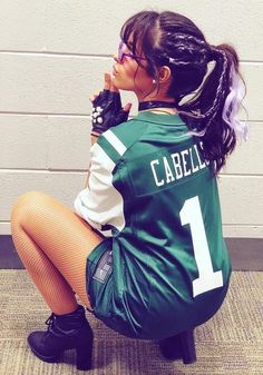 a woman sitting on the ground with her hands in her mouth and wearing a football jersey