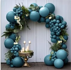 a wreath made out of balloons and greenery with candles on a table in front of a white wall