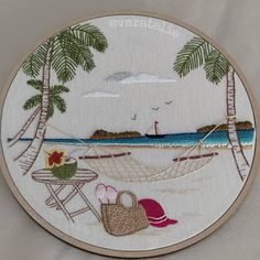 an embroidered wall hanging depicting a beach scene with hammock, chairs and palm trees