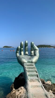 a hand statue sitting on top of a rock near the ocean