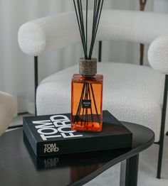 an orange bottle with reeds sitting on top of a black table next to a white chair