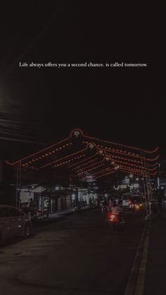 a street with cars parked on the side and lights strung over it at night time