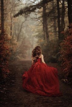 a woman in a red dress is walking down a path through the woods with trees