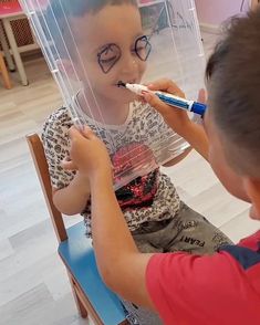 a young boy is brushing his teeth while sitting in a chair with another child on the other side