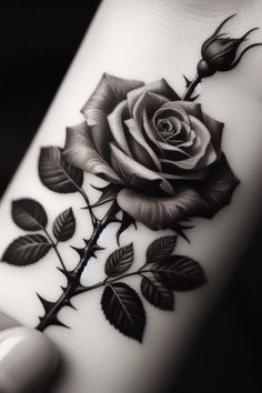 a rose tattoo on the wrist is shown in black and white colors, with leaves around it