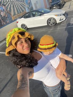 a woman holding a child in her arms and wearing a crocheted hat with a hamburger on it