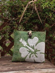 a green and white purse sitting on top of a wooden bench next to a bush