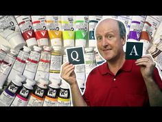 a man holding up a card with the letter q on it in front of paint bottles