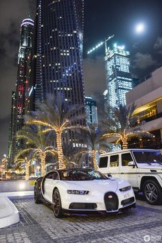 two bugatti cars parked in front of a tall building at night with palm trees