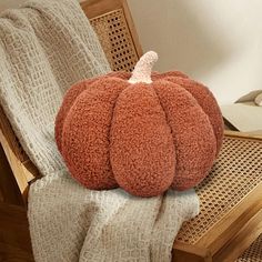 an orange pumpkin sitting on top of a chair next to a white blanket and pillow