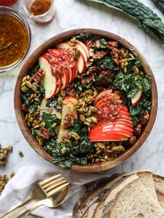 a wooden bowl filled with sliced apples and spinach next to some slices of bread