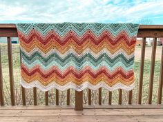 a crocheted blanket is hanging on a wooden rail in front of a grassy field