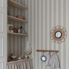 a kitchen with striped walls and white cupboards next to a shelf filled with pots and pans