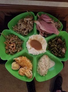 a green plate filled with different types of food on top of a wooden table next to a person's feet